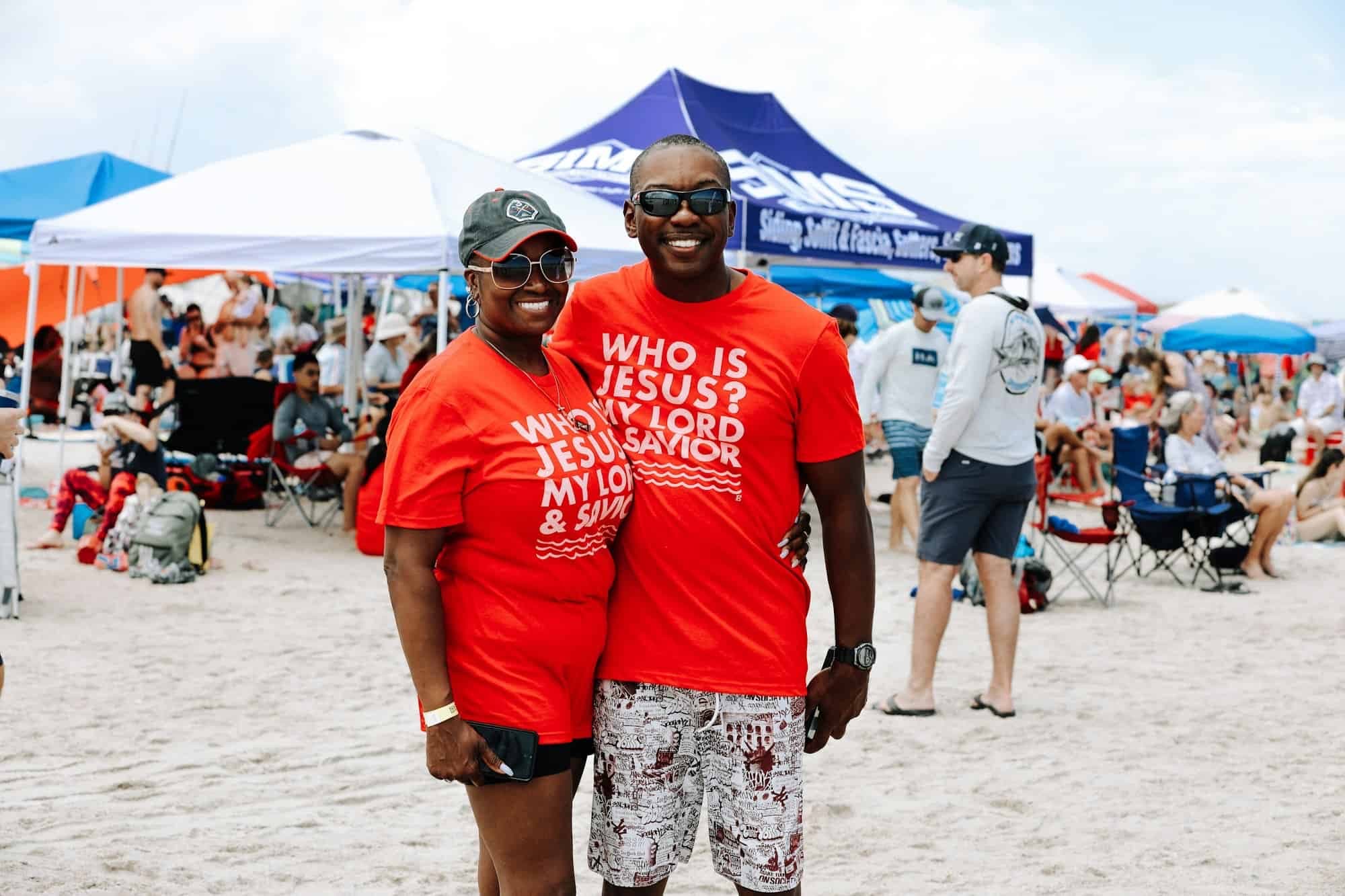 A smiling couple in Who Is Jesus shirts at Beach Baptism