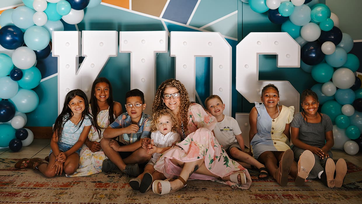 An Eleven22 Kids leader sitting with kids in front of the KIDS marquee sign
