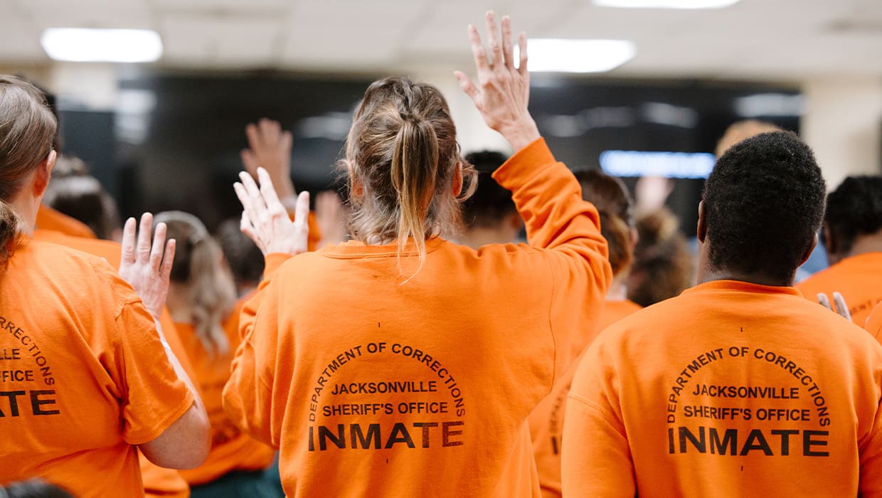Men and women worshipping with hands raised inside a correctional facility