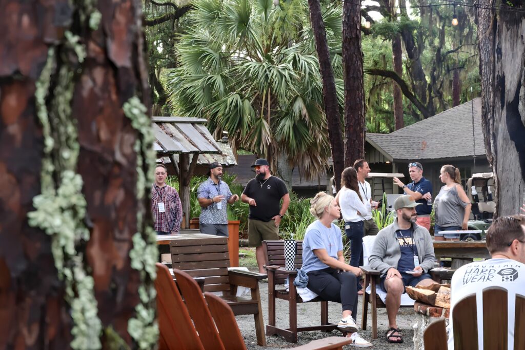Group of parents engaged in conversation at the Eleven22 Retreat Center, surrounded by trees and outdoor seating, highlighting community and support for discussing identity topics with preteens.