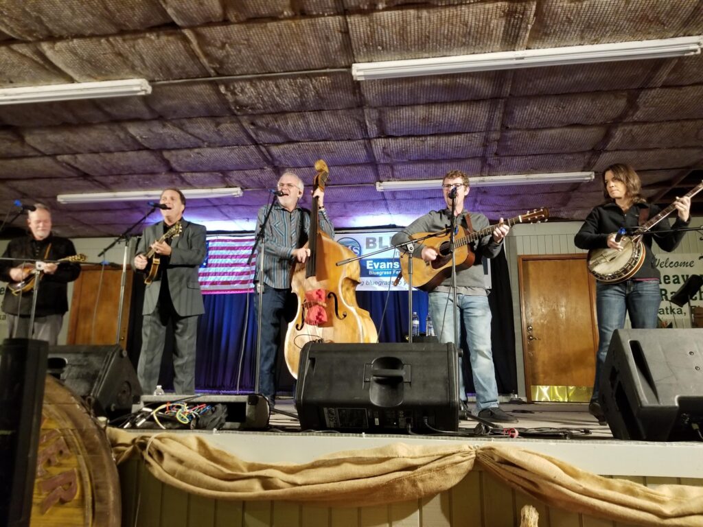 Bluegrass band performing live on stage at the 2026 Palatka Bluegrass Festival, featuring musicians with various instruments, including a banjo, guitar, and mandolin, in a family-friendly concert setting.