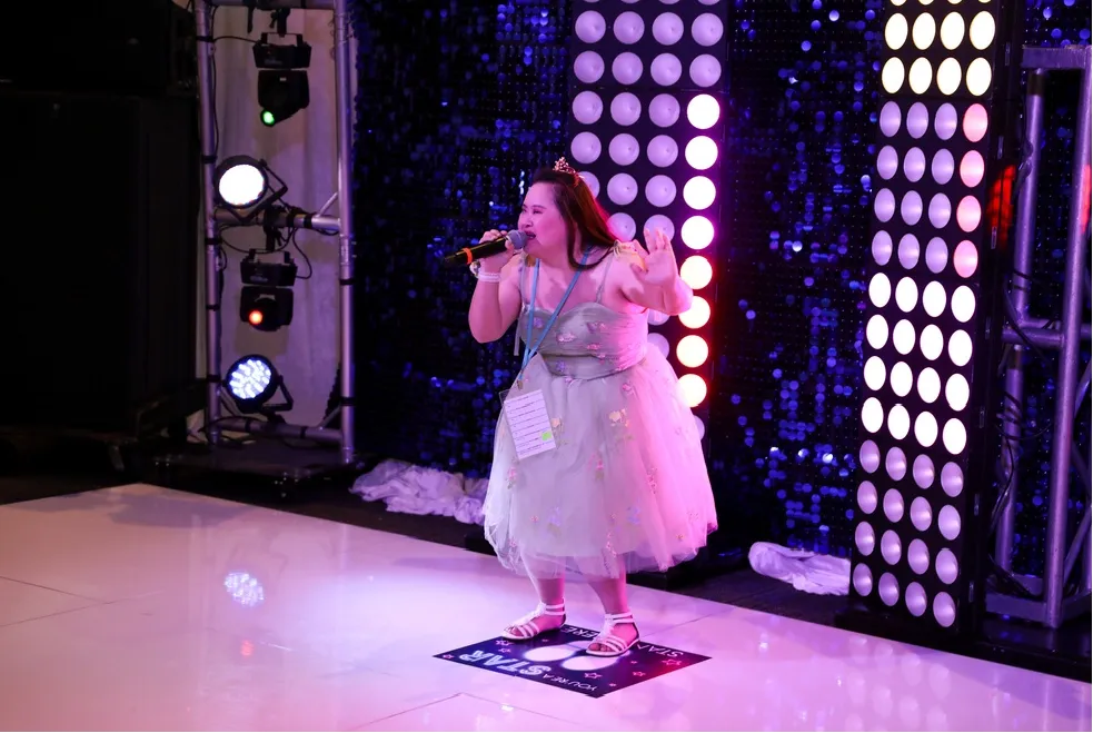 Girl in a light green dress singing on stage at Night to Shine event, surrounded by colorful lights and a joyful atmosphere.